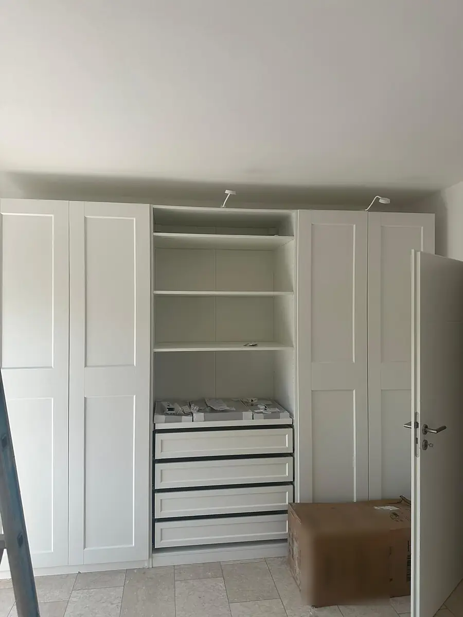 Schrankwand mit Rahmentüren und offenem Mittelteil mit Böden und Schubladen, davor ein verpackter Karton