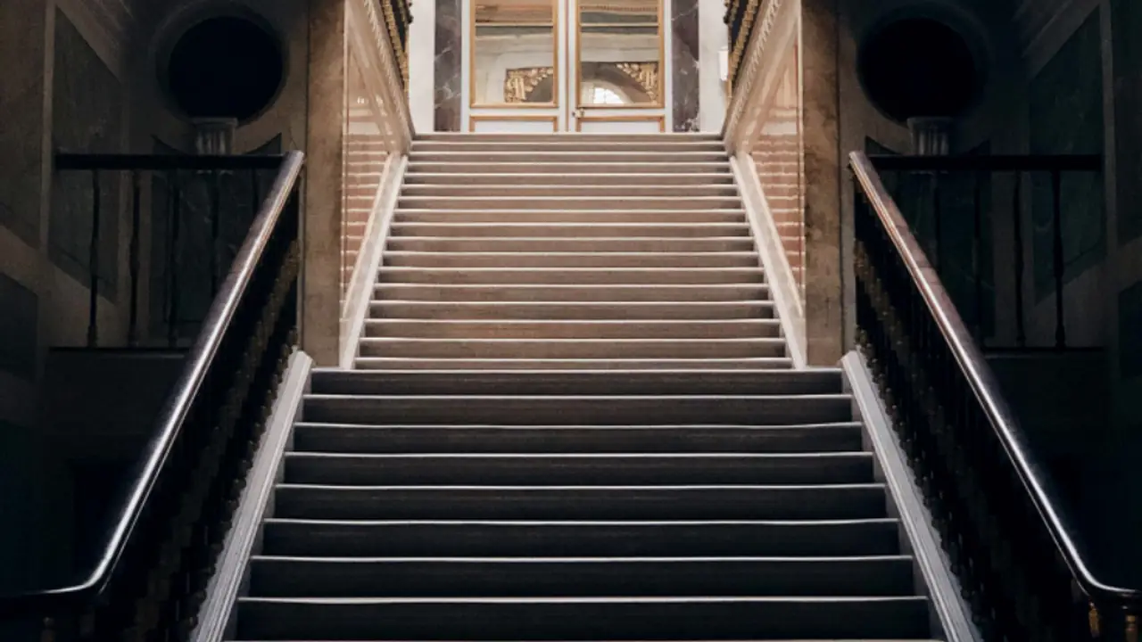 Lange Treppe in einem hohen Altbau-Treppenhaus mit Tür am oberen Ende