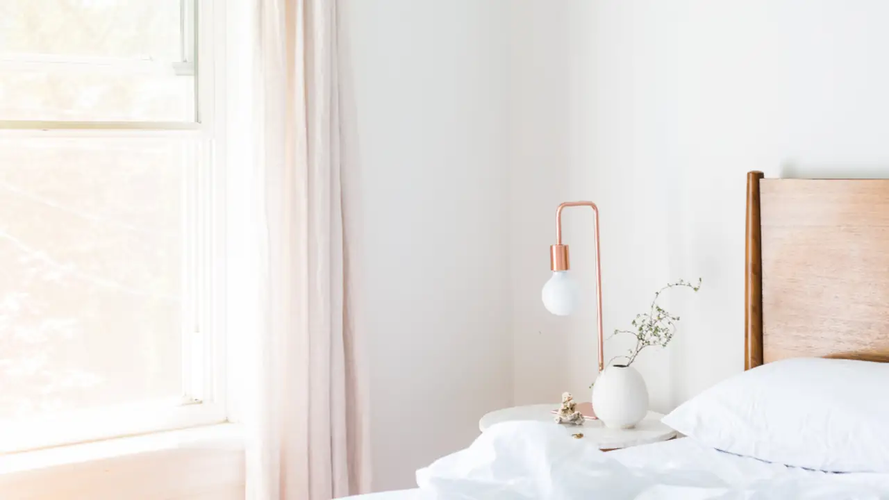 Helles, schlicht eingerichtetes Zimmer mit Bett, Leuchte und Fenster